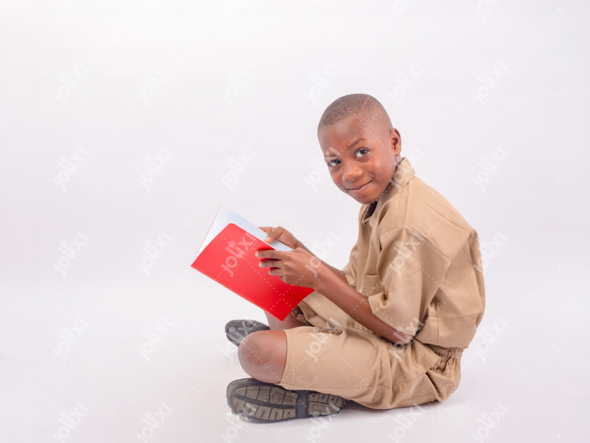 Un écolier africain souriant assis en uniforme scolaire tenant son cahier  sur un fond blanc - Photo #3611 - Jolixi